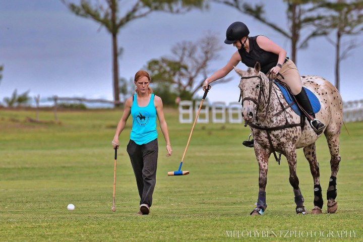 A person on horseback attempts to hit a ball with a mallet, with another person walking beside.