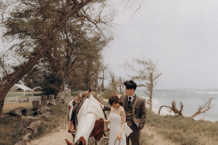 Bride and groom with a horse on a sandy path by the sea.