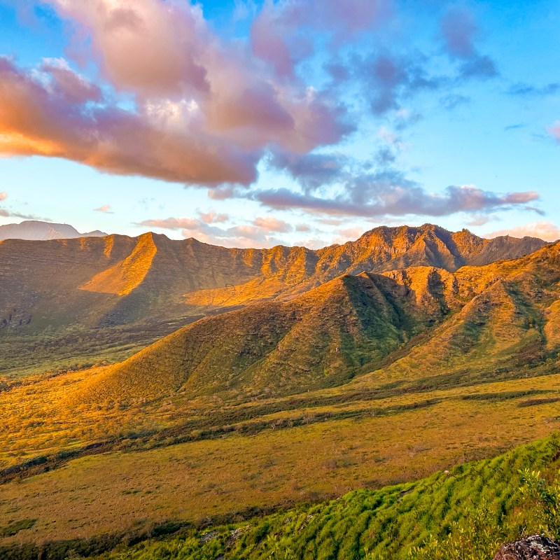 Mountain range at sunset with golden light and cloudy sky.