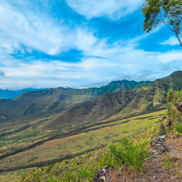 Mountain landscape with green valleys, trees, and blue sky with clouds.