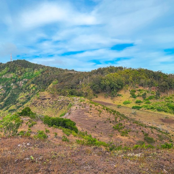 A scenic view of a green mountainside under a blue sky with scattered clouds.